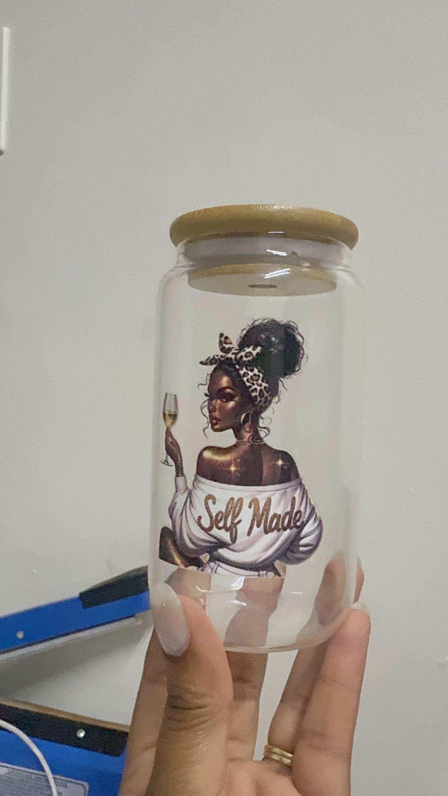 Hand holding a clear glass jar with a wooden lid, featuring a graphic of a "Self Made" woman holding a champagne glass.